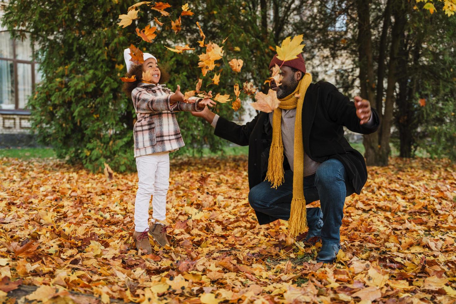 Black grandfather and granddaughter having fun with leaves in autumn park photo