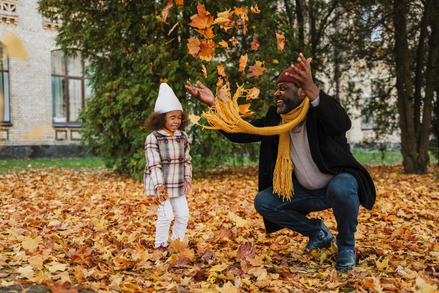 Abuelo negro y nieta burlándose con hojas caídas en el parque de otoño foto