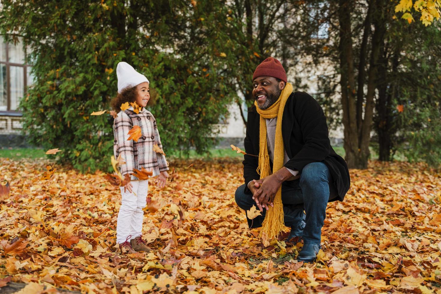 Abuelo negro y nieta burlándose con hojas caídas en el parque de otoño foto