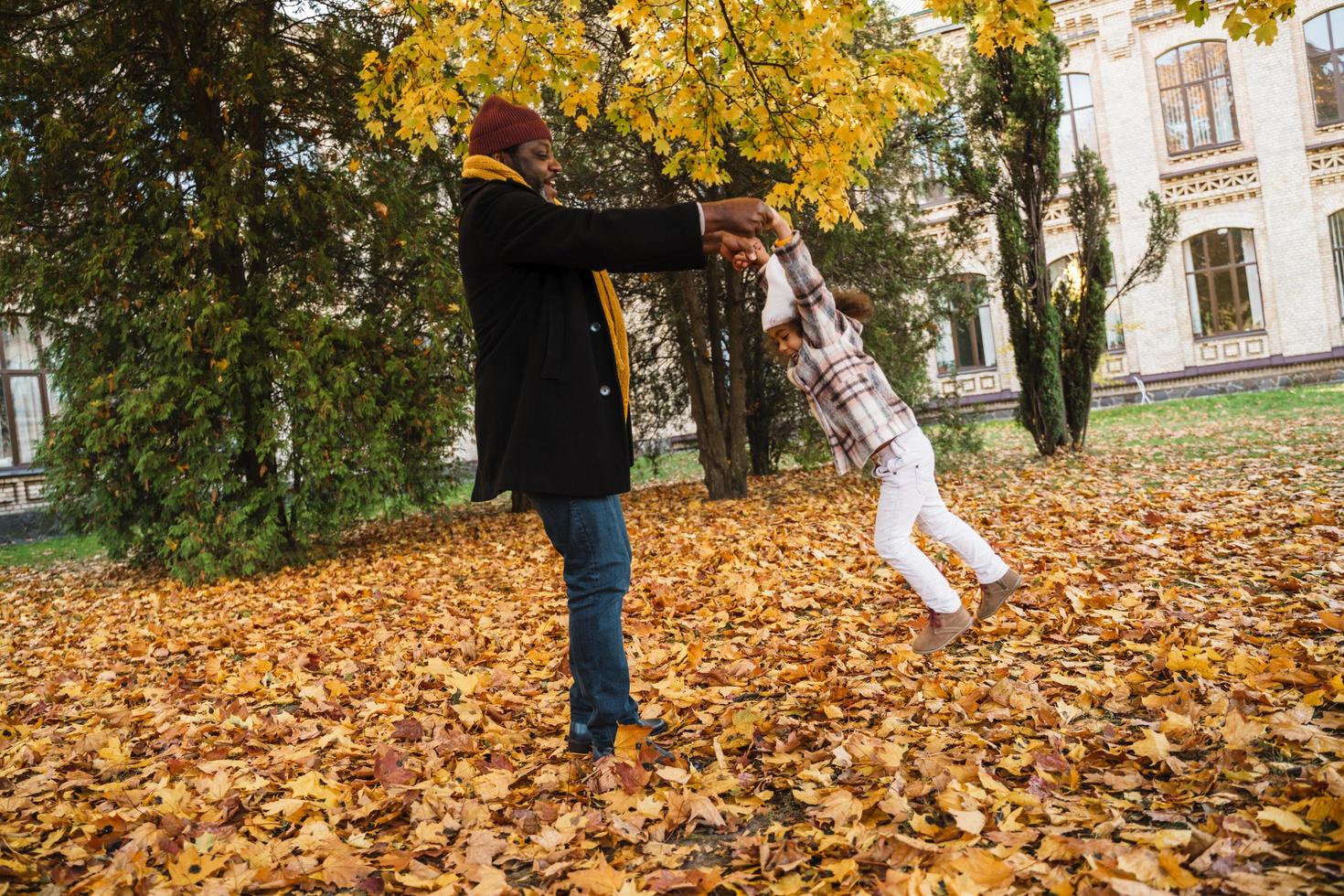 Black grandfather and granddaughter playing together in autumn park with leaves photo