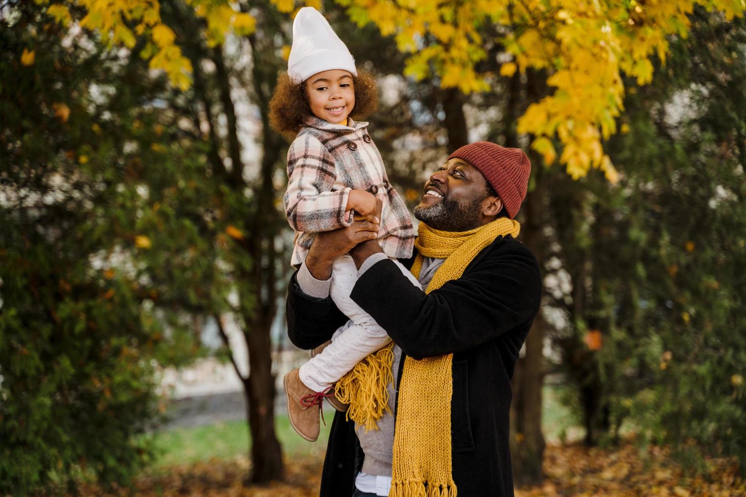 Chica negra divirtiéndose y sentada en el cuello de su abuelo en el parque de otoño foto