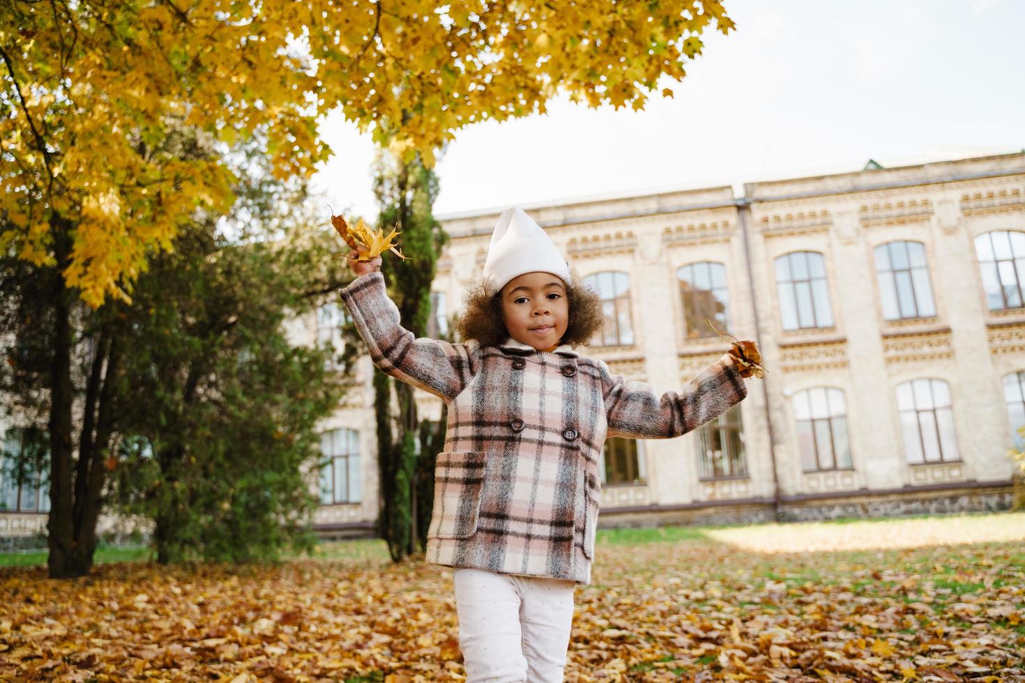 negro, niña, llevando, abrigo, burlarse, con, hojas caídas, en, otoño, parque foto