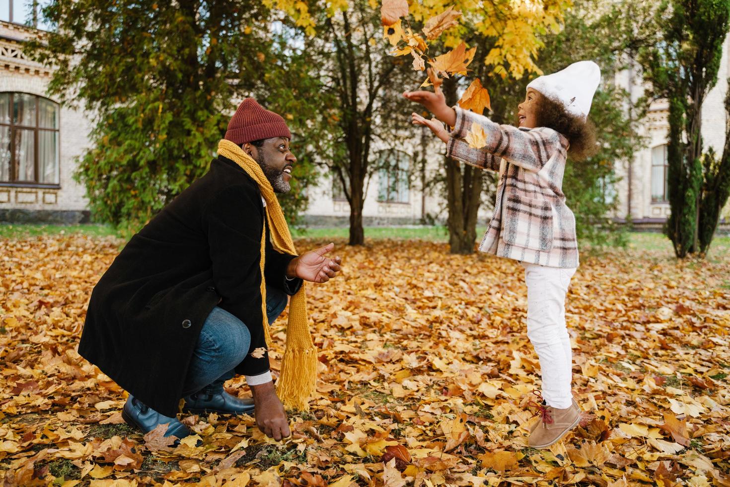 Abuelo negro y nieta burlándose con hojas caídas en el parque de otoño foto