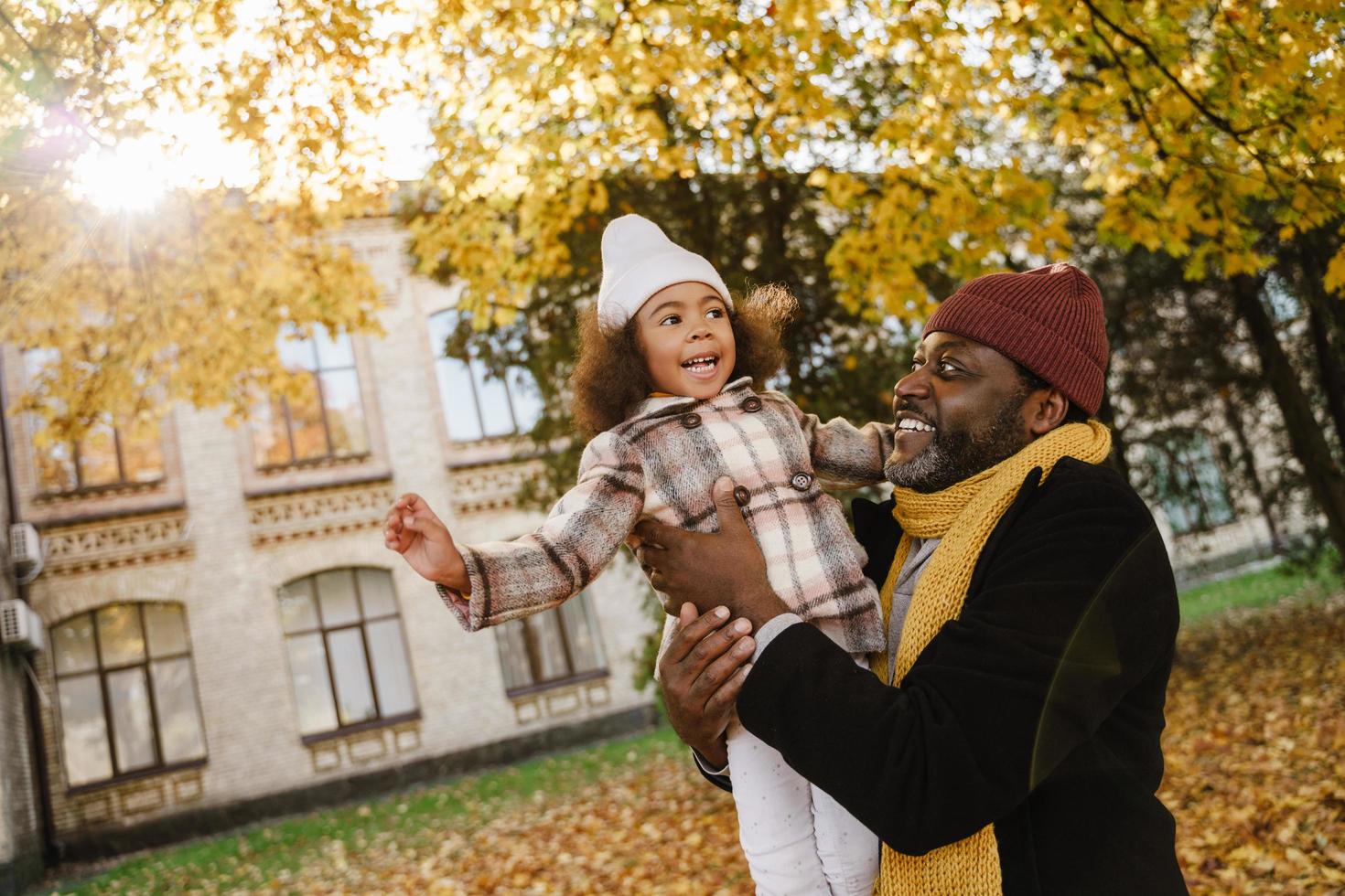 Black grandfather and granddaughter playing together in autumn park and having fun photo