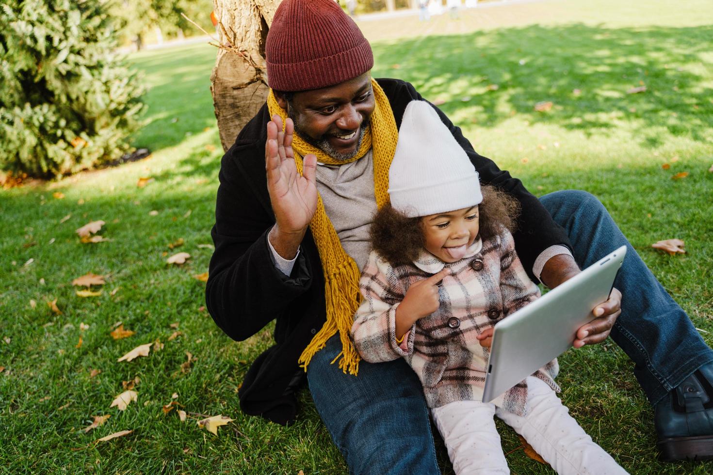 Black grandfather and granddaughter using tablet computer while sitting in a park photo
