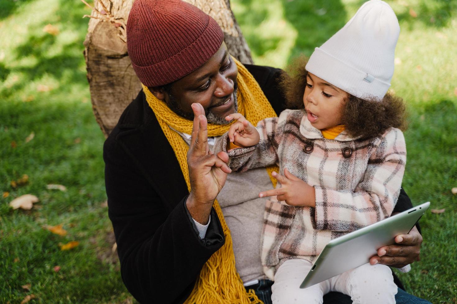Black grandfather and granddaughter using tablet computer together sitting in park photo
