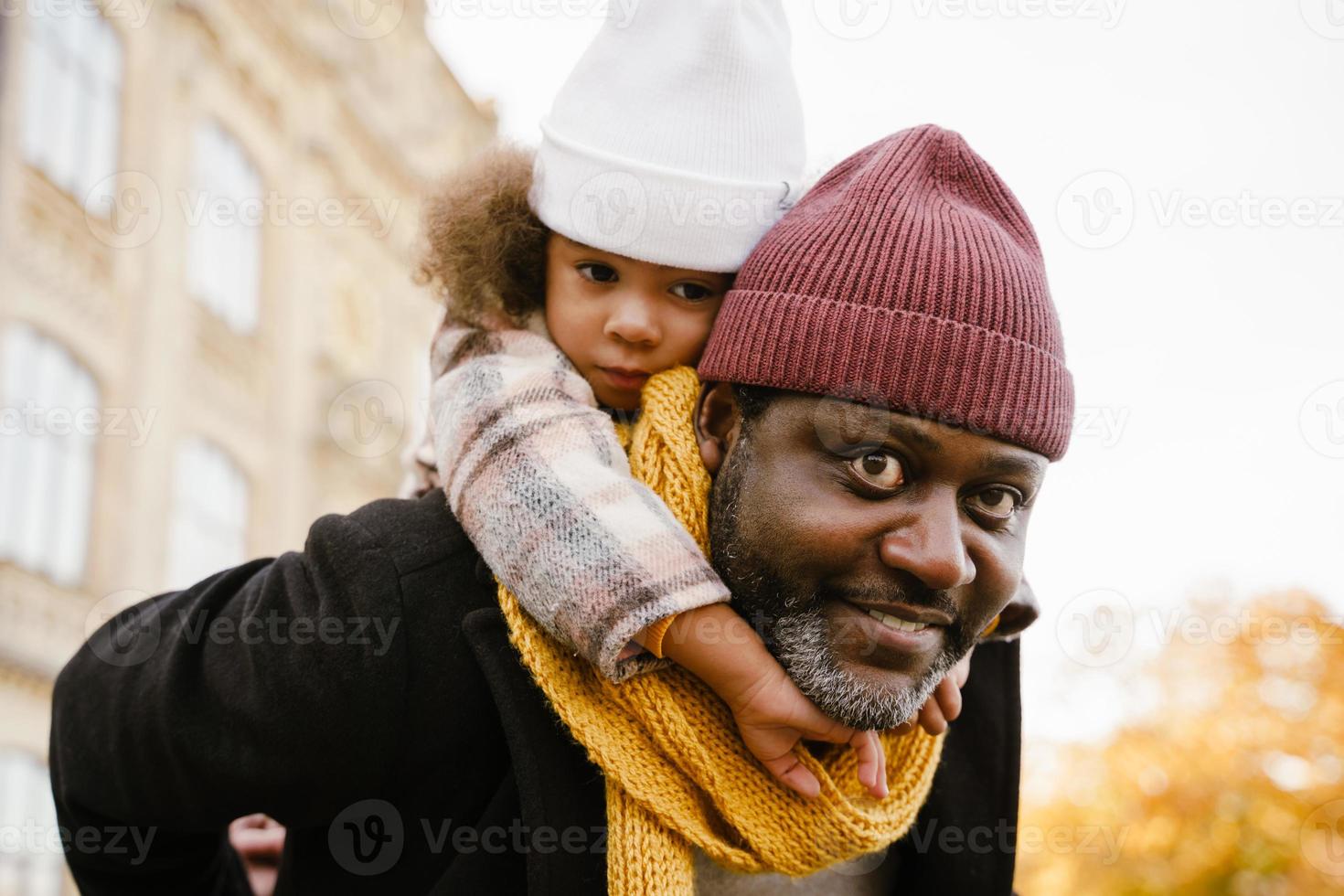 Black girl having fun and sitting on neck of her grandfather in park in autumn photo