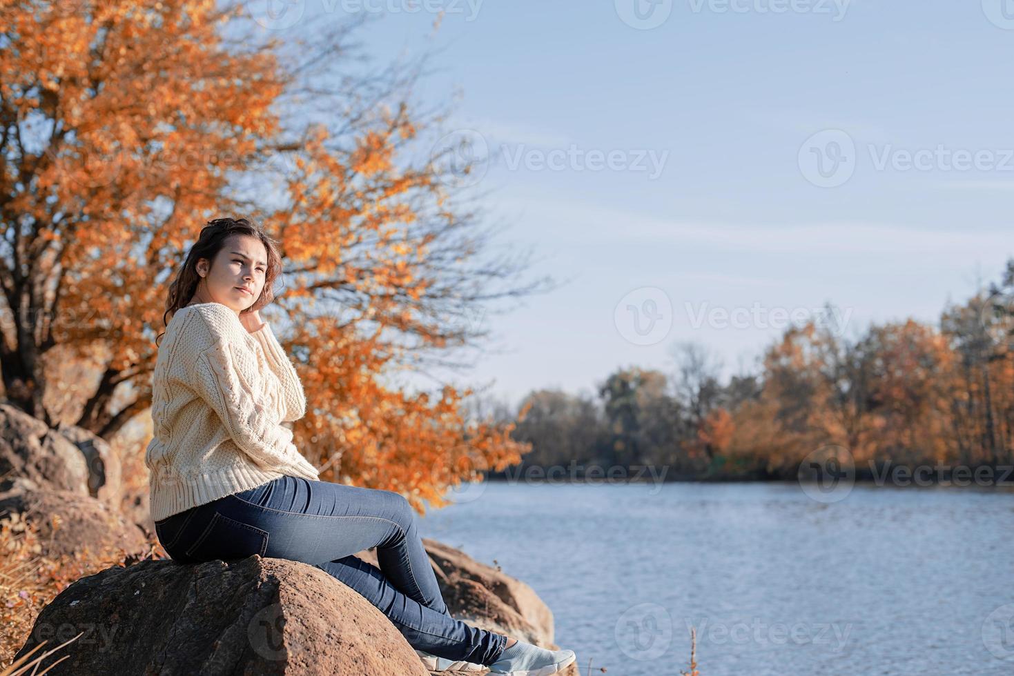 Thoughtful romantic woman sitting on rocks on the river bank in sunset in autumn day photo