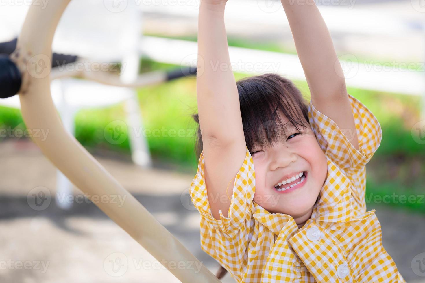 ejercicio de niño feliz en el patio de recreo. chica asiática con camisetas amarillas es feliz sonriendo dulce. niño sano tiene 5 años. de cerca. foto