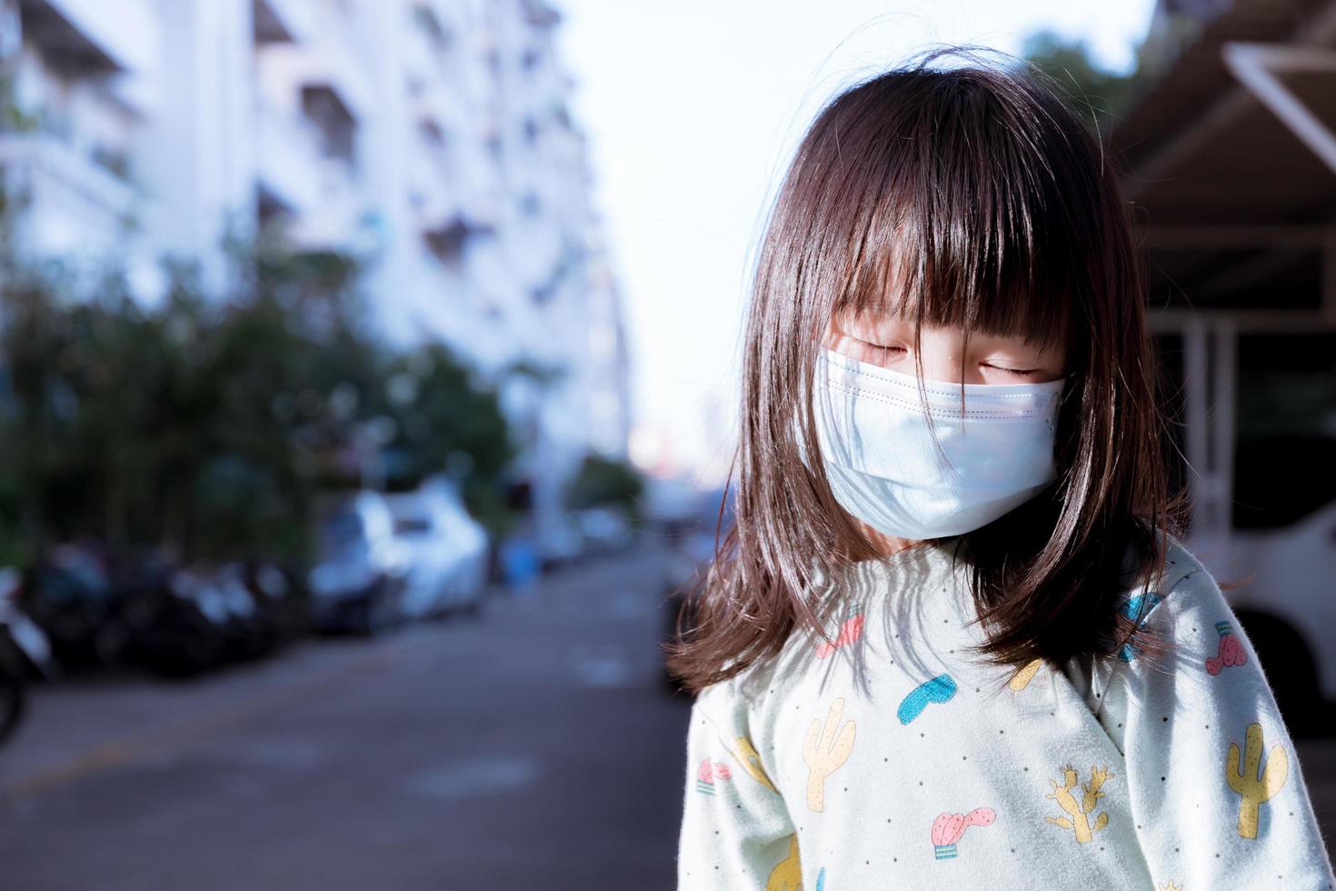 Children wear a blue surgical face mask. Child closes his eyes while taking a picture. Take a walk outside. During winter in Thailand. Kid aged 3-4 years old. photo