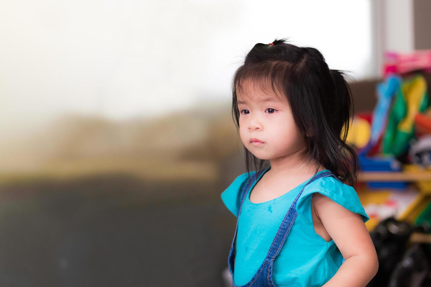 Portrait Asian child girl is crying and rim red eyes. Kid has tears in her eyes. Cute little girl is sad and looks on the thought of something. Baby aged 3 years and 5 month. In the house. photo