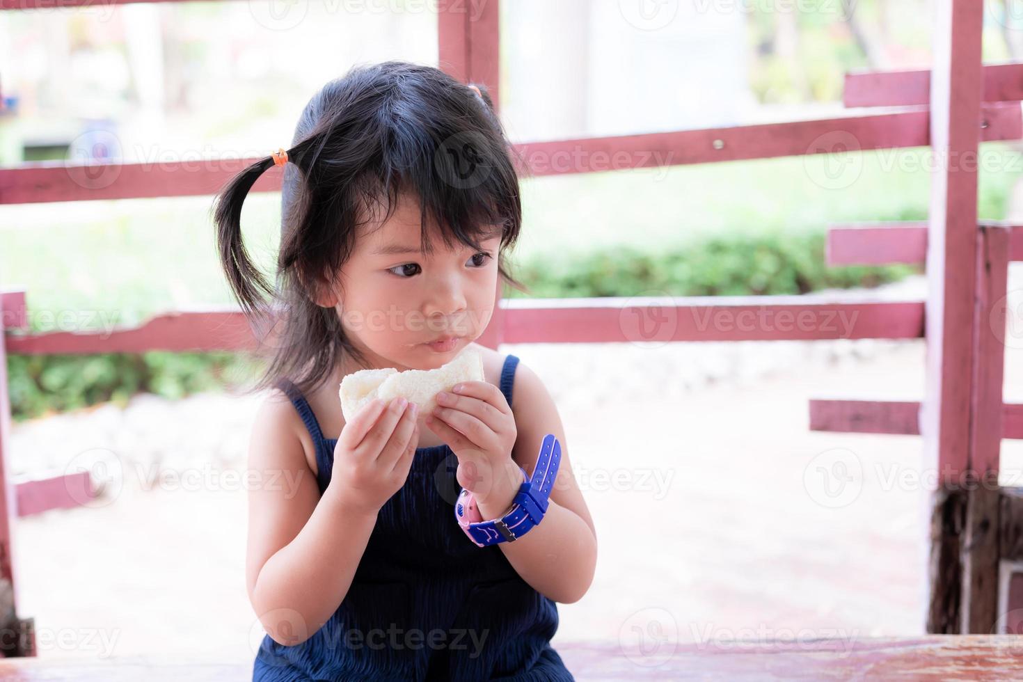 adorable chica asiática comiendo pan mientras viaja. lindo niño tiene hambre. los niños visten lindas ropas oscuras. el niño tiene 3 años. copie el espacio. foto