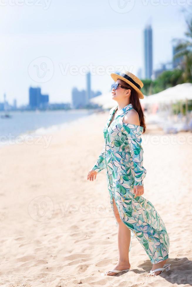 imagen vertical. hermosa mujer de pie relajándose en la playa. Hora de verano. persona feliz con gafas de sol y sombreros de paja marrón. dulce sonrisa. foto