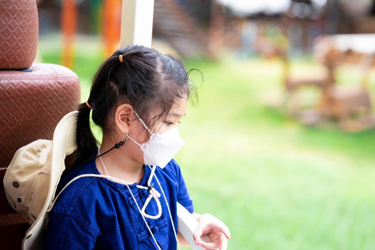 Child wear white face masks 4D shapes to prevent spread of virus and prevent PM2.5 air pollution. Cute kid sits down after playing until her is tired, girl is feeling sad. photo