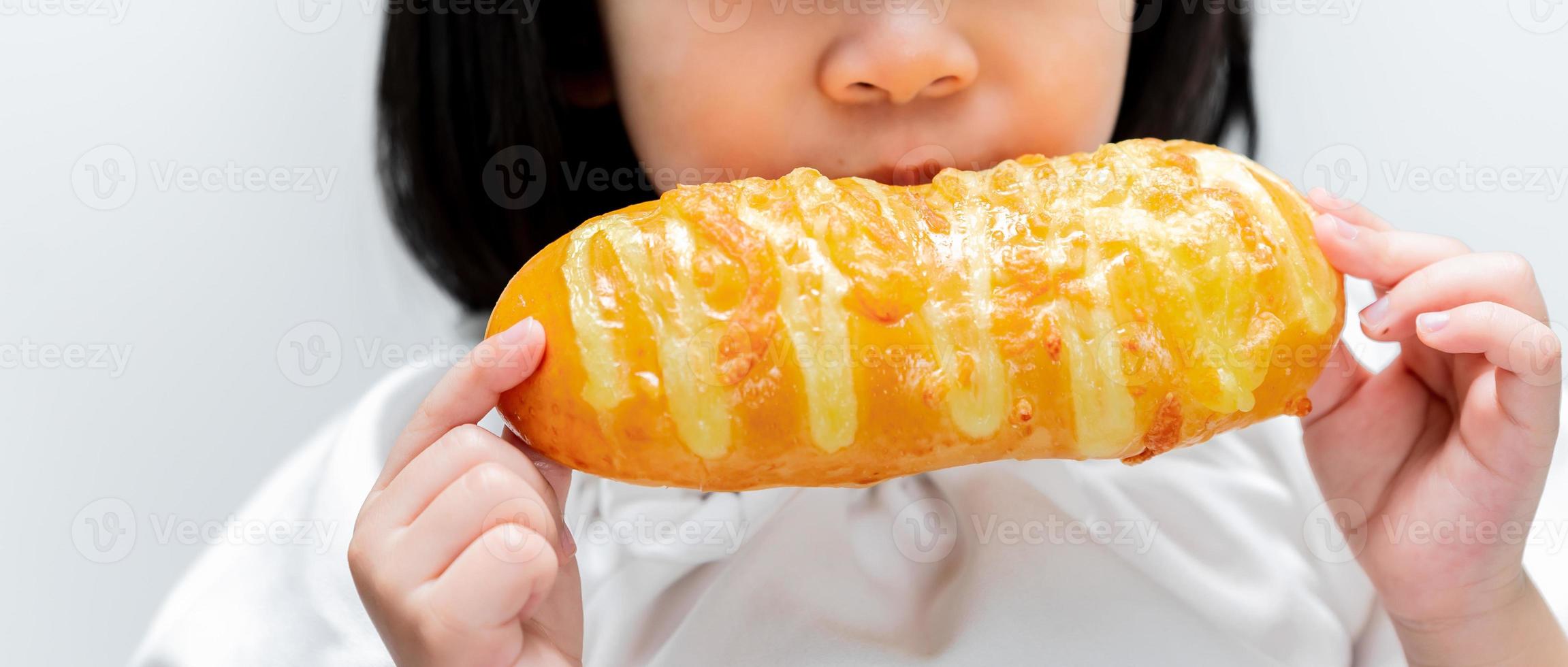 chica asiática comiendo tostadas dulces. niño feliz sosteniendo un hermoso bollo largo en sus manos. foto