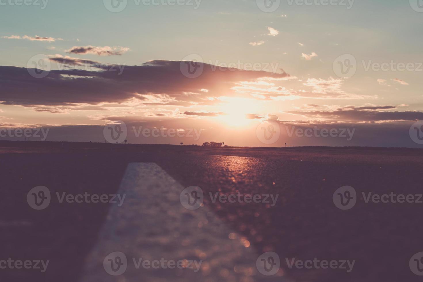 el atardecer o el amanecer del sol sobre un camino que se adentra en la distancia. los rayos del sol, abriéndose paso a través de las nubes sobre la carretera. foto