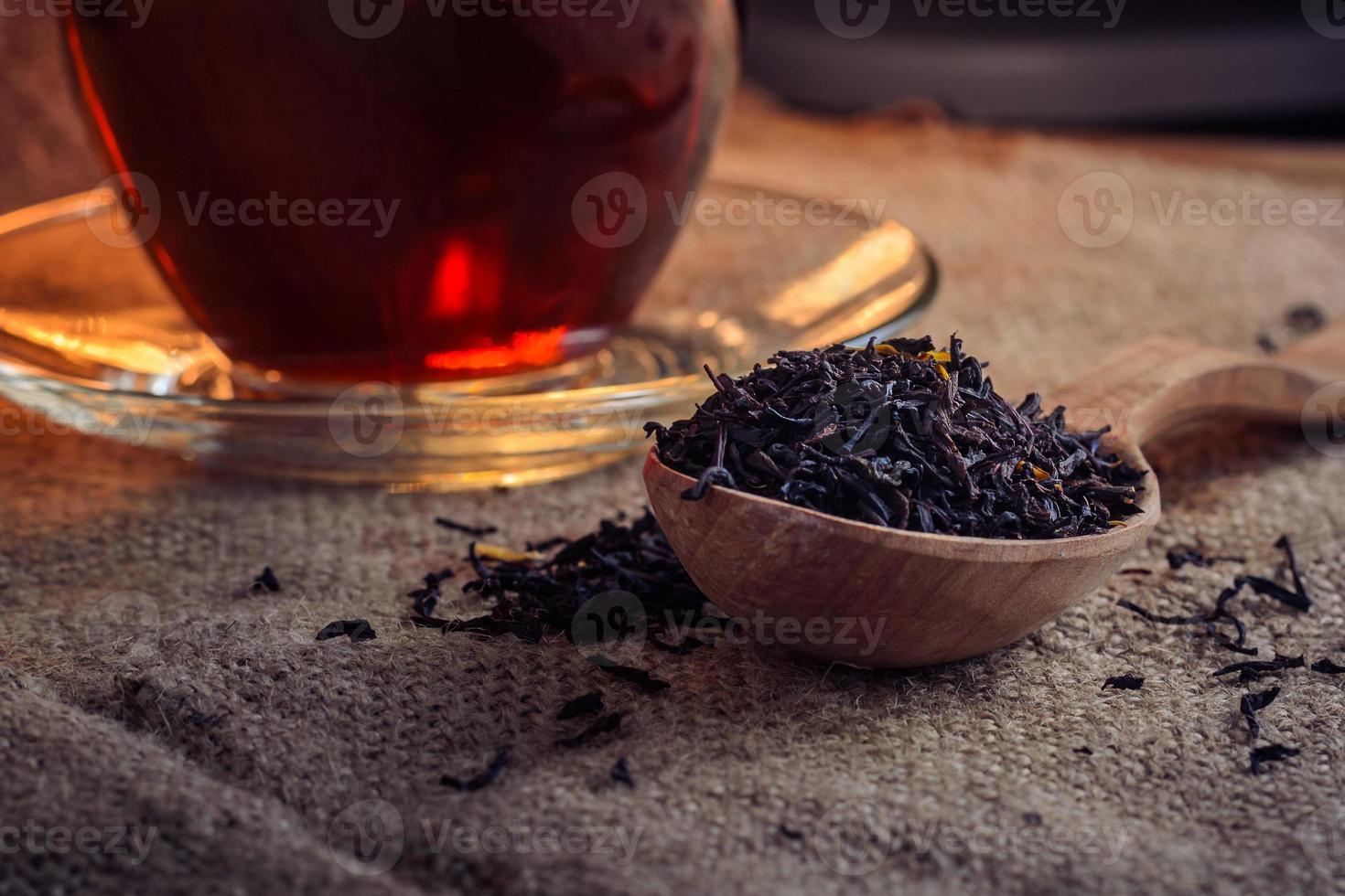 Secar las hojas de té en una cuchara de madera y elaborado en una taza de té de vidrio sobre un fondo de arpillera foto