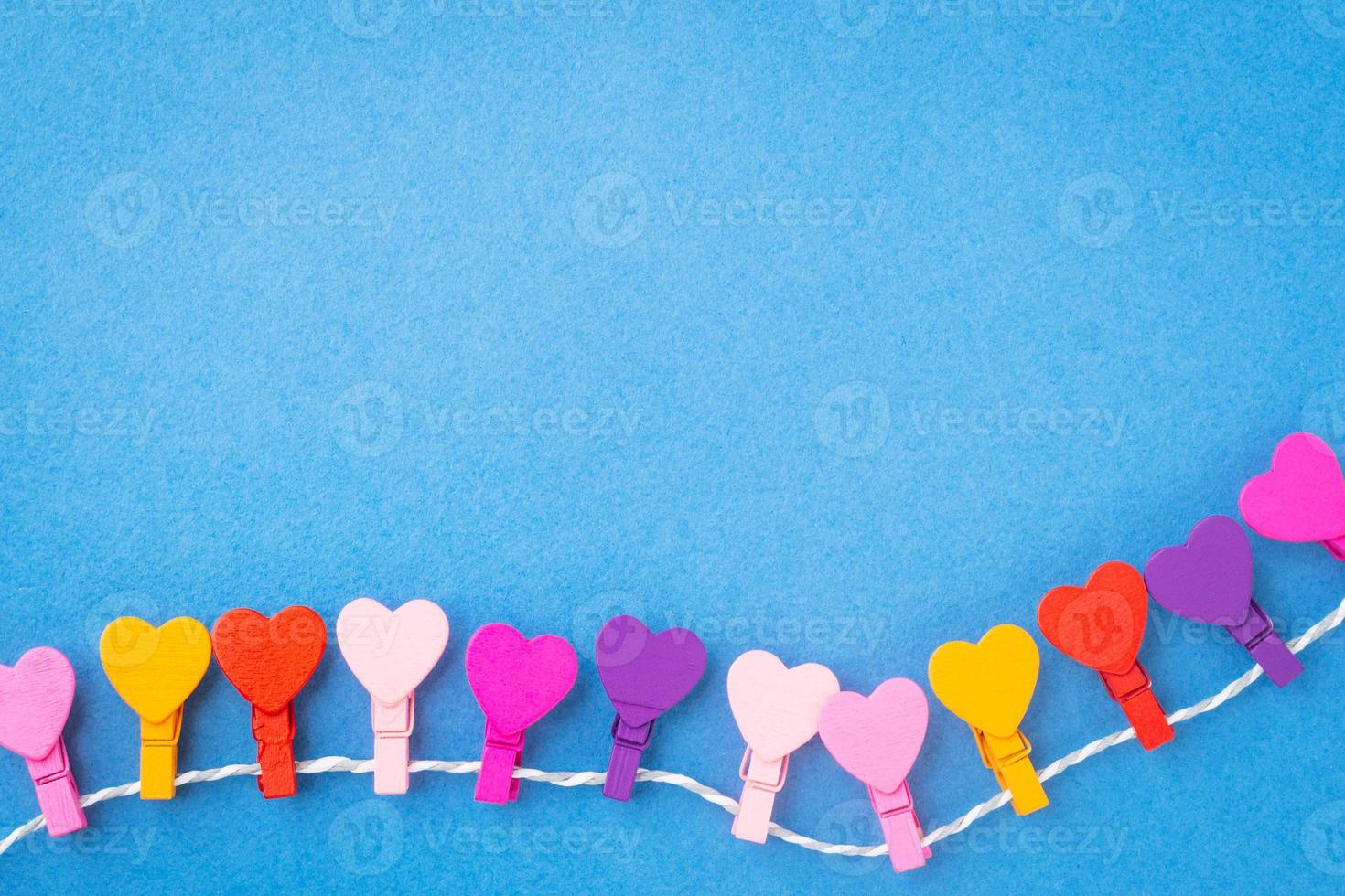 A frame of colored wooden hearts hanging on a rope on a blue background. photo