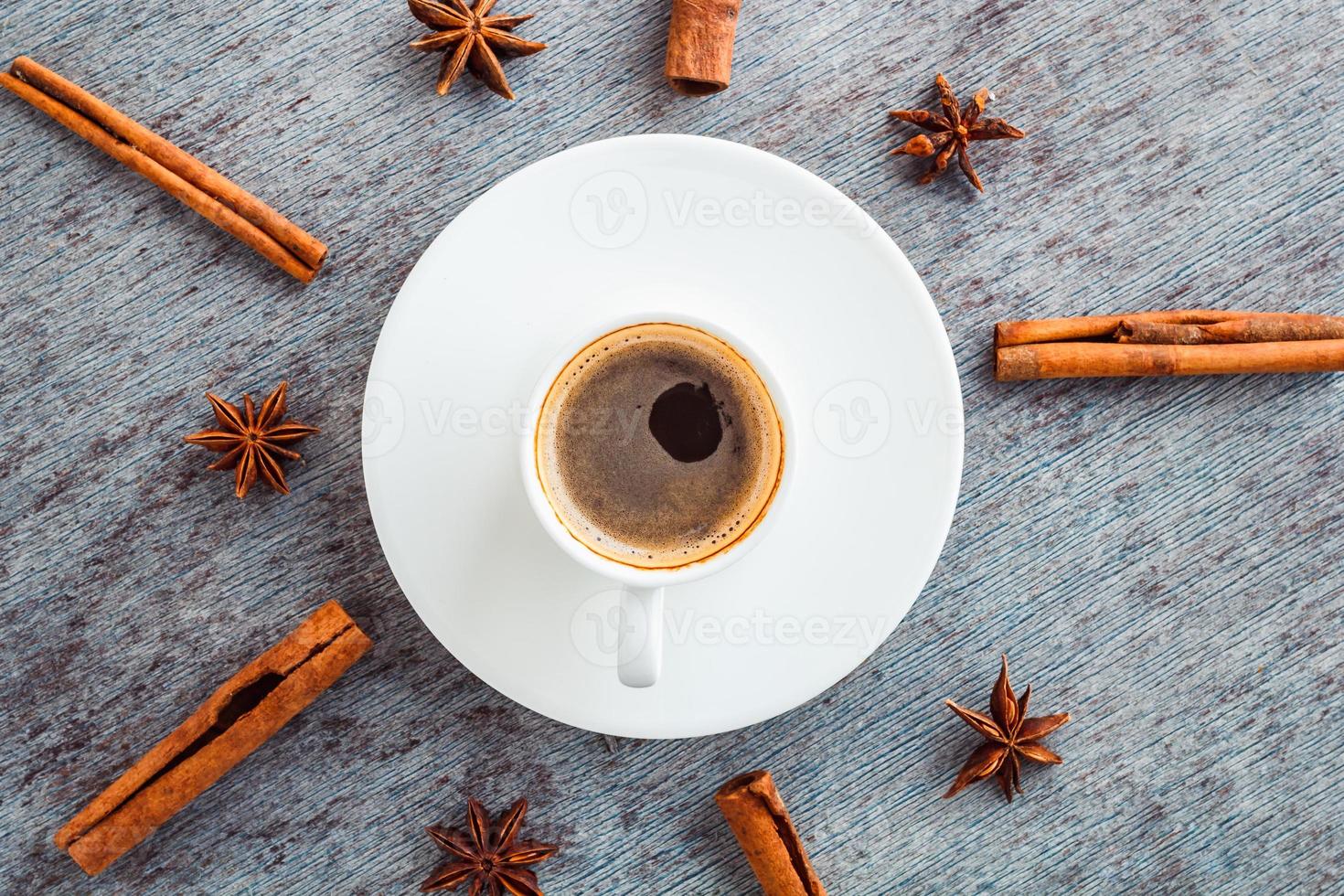 una taza de café en un plato y brotes de canela y anís esparcidos alrededor de un palito foto