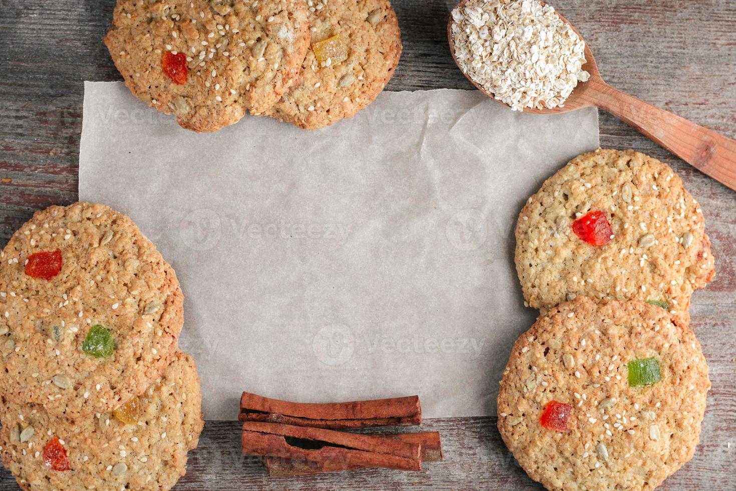 Hornear, galletas de avena en un piso plano con una cuchara de madera y palitos de canela sobre papel para hornear sobre una mesa de madera en estilo rústico foto