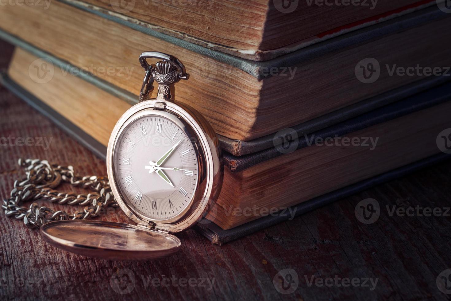 Reloj de bolsillo vintage con cadena y libros antiguos sobre un fondo de madera. imagen teñida en clave baja foto