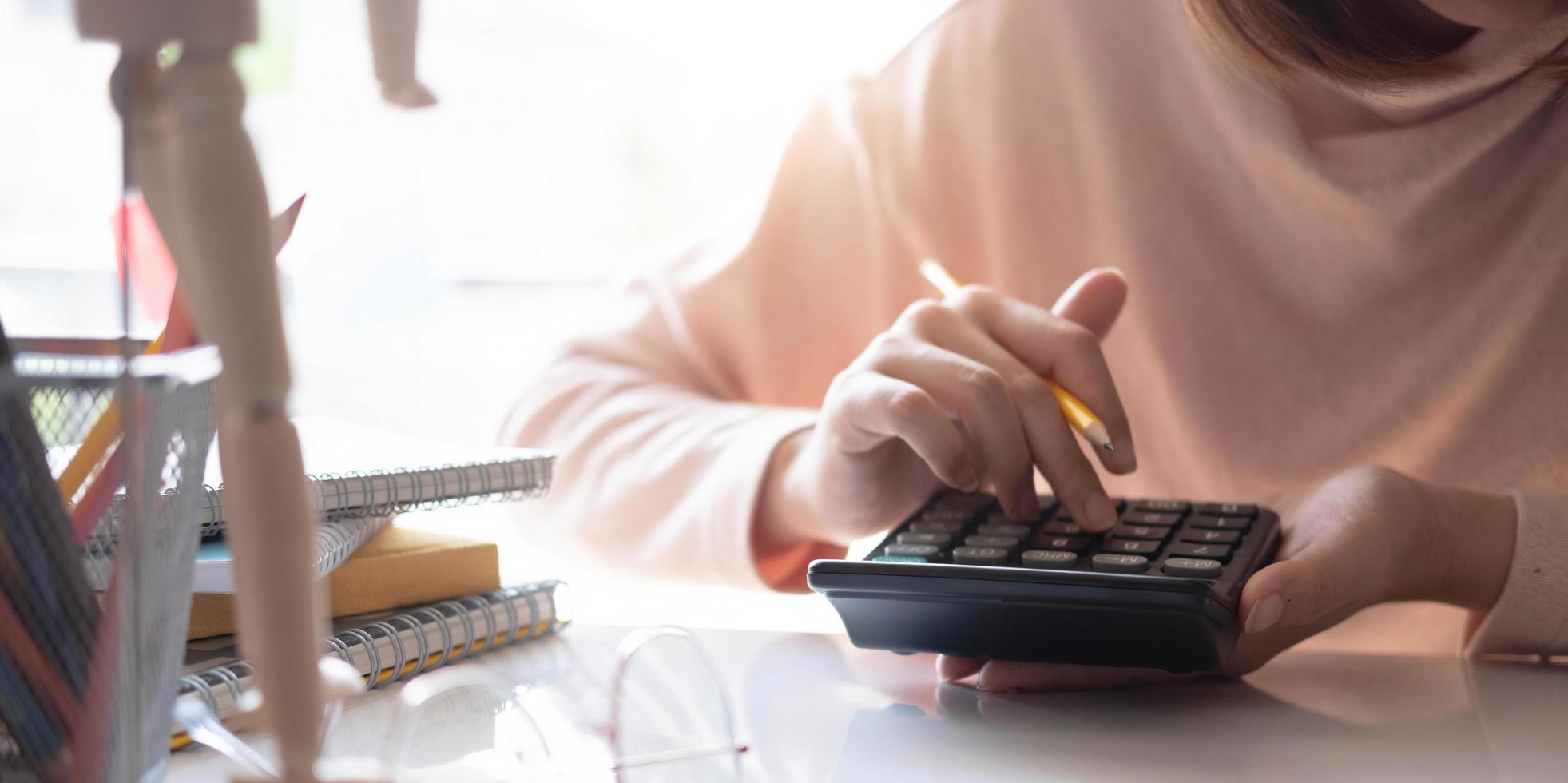 woman hand working with calculator and holding yellow pencil with nature green leaves background. photo