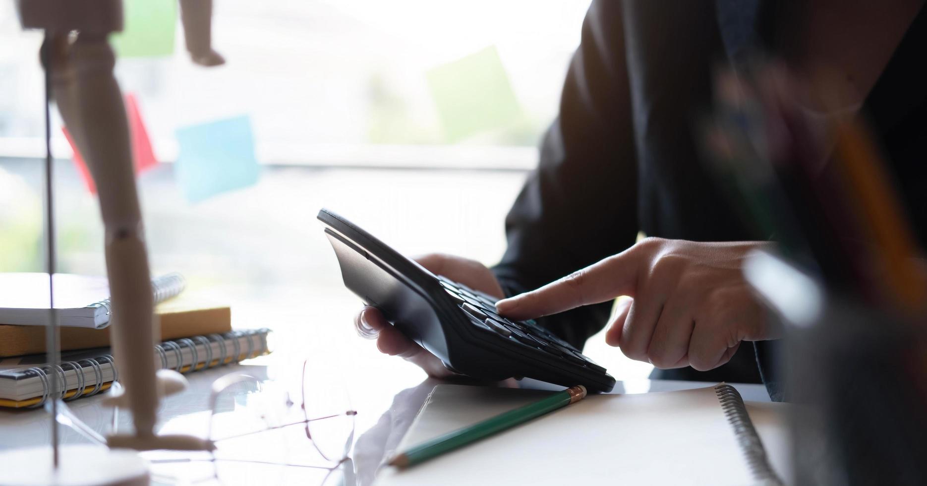 empresaria trabajando en el cálculo de estadísticas de ingresos presupuestarios usando la calculadora sosteniendo un bolígrafo apuntando al gráfico en la oficina. foto