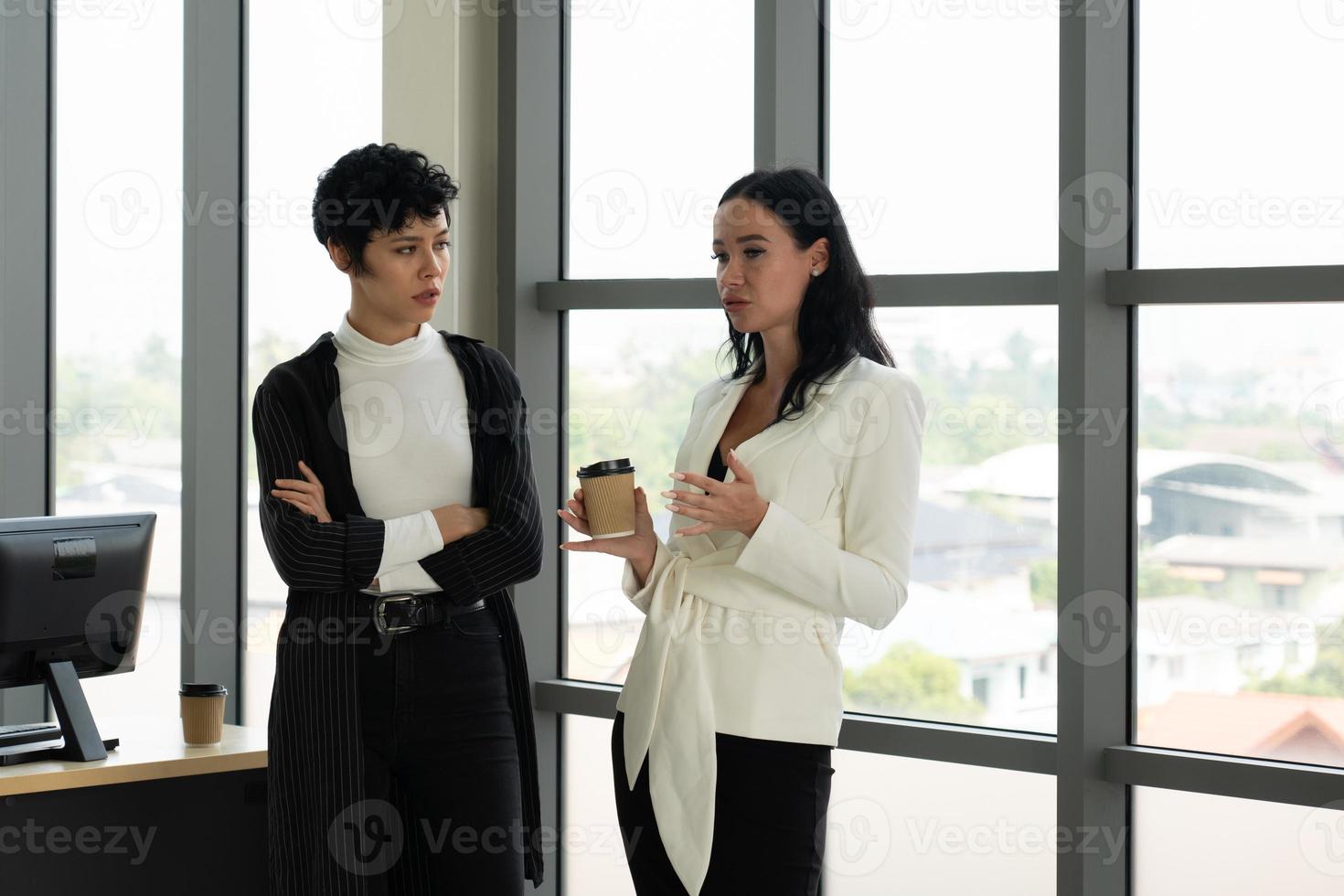 two caucasian businesswoman standing near window talking about work in office. business concept photo