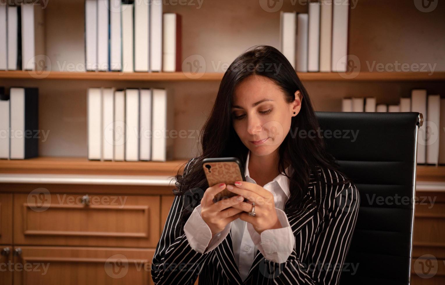 Retrato de joven empresaria caucásica hermosa leyendo el correo electrónico en el teléfono inteligente en la oficina. concepto de negocio foto