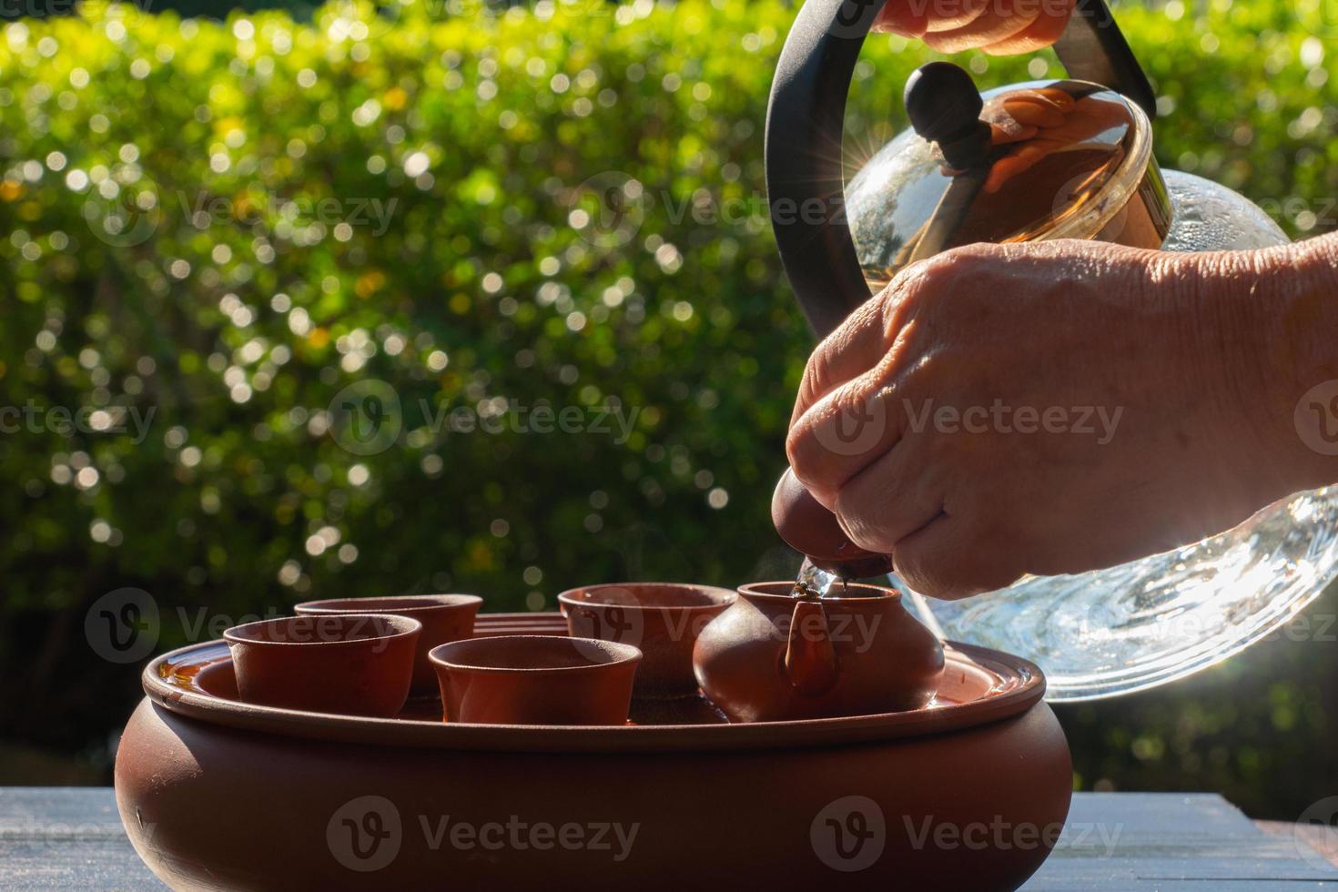 people pouring hot water into small kettle and cup to make chinese traditional tea in garden photo