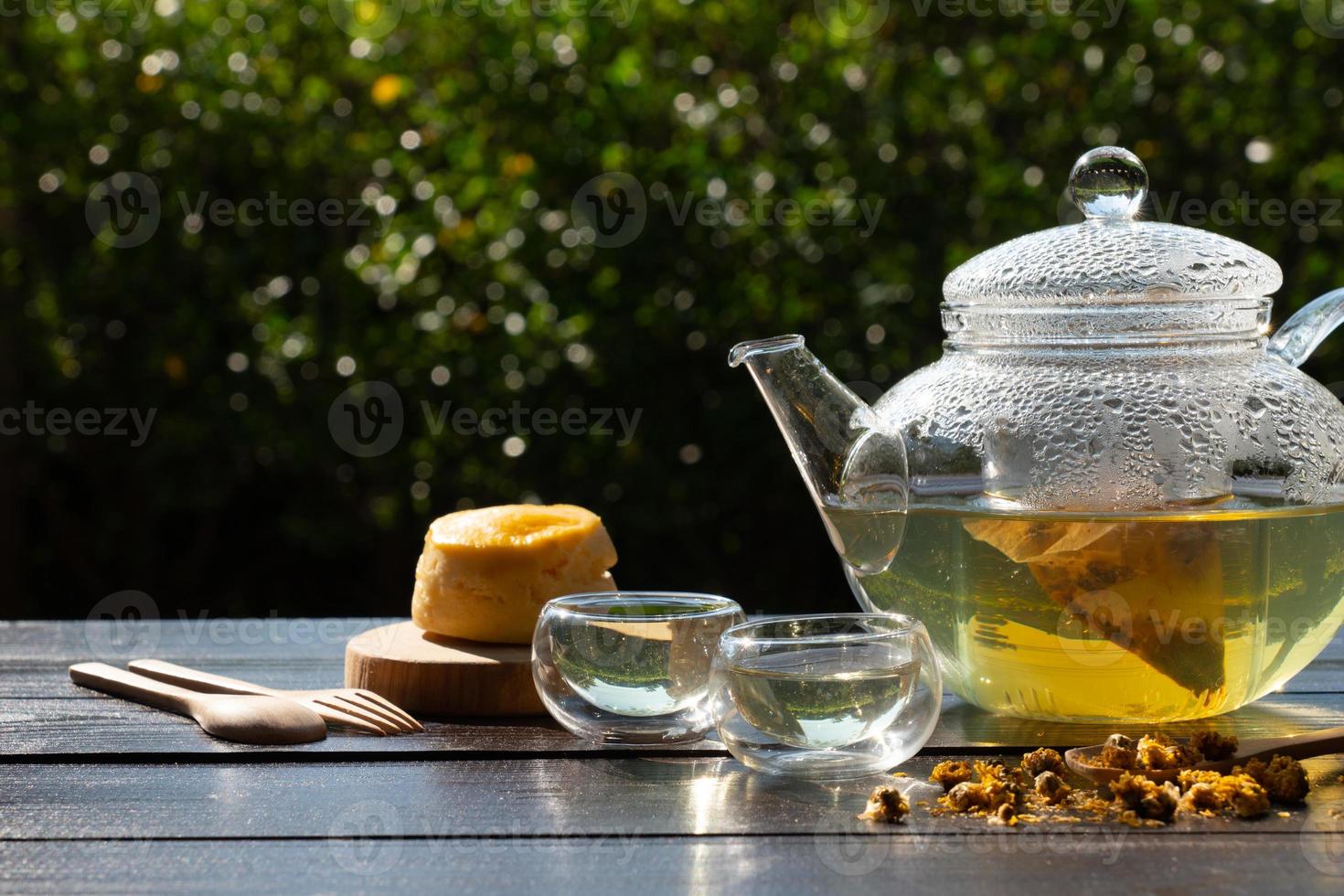 Té de crisantemo en tetera de vidrio con taza y bollo para la fiesta del té de la tarde en el jardín foto