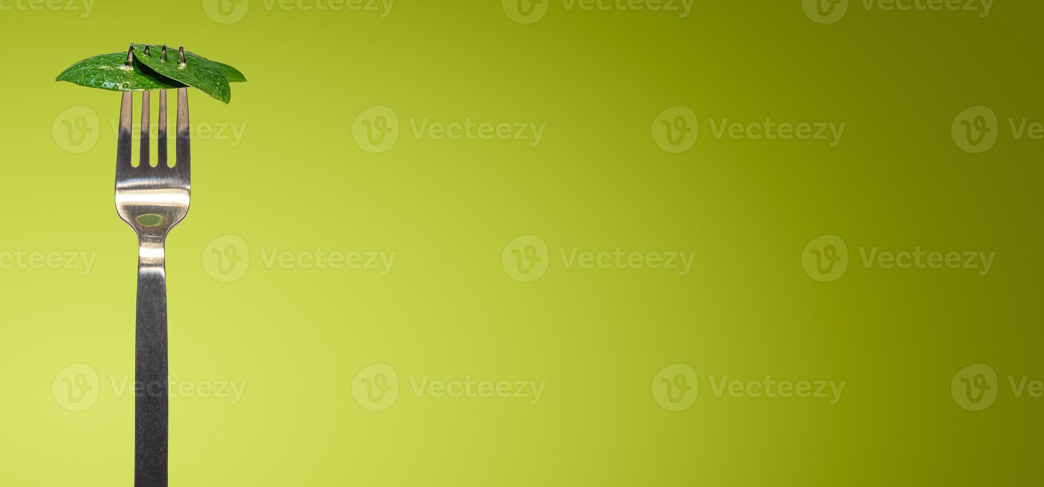 Banner with green fresh leaves picked by a fork for eating as new vegan food isolated at green smooth gradient background with copy space for text, closeup, details photo