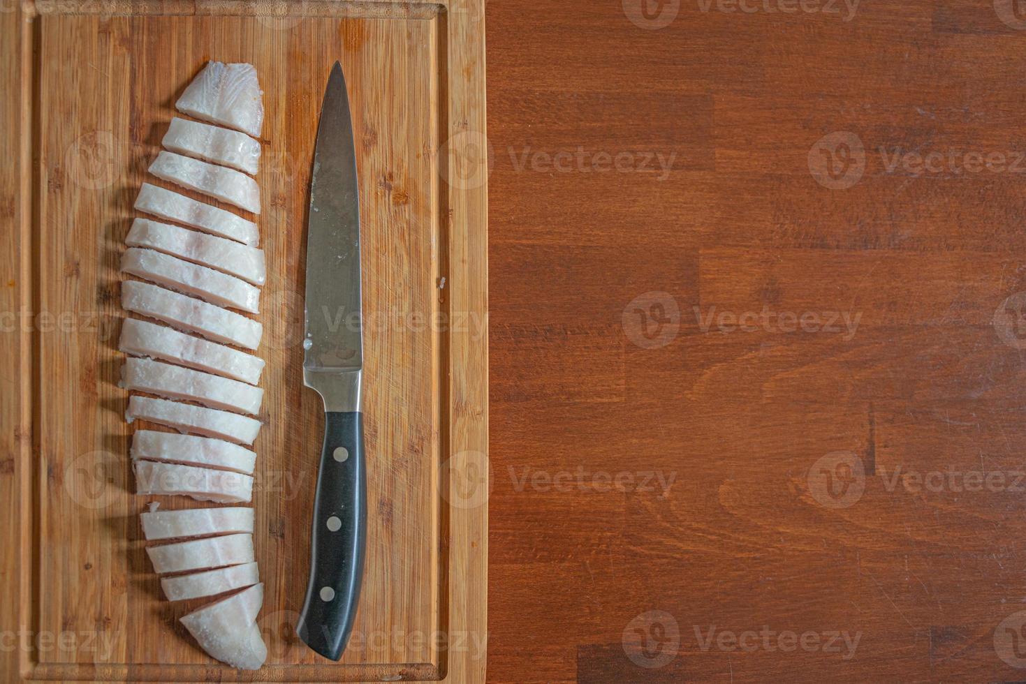 Pescado medio congelado en una tabla de madera cortada en rodajas finas con un cuchillo grande, detalles, primer plano, con espacio de copia como un plato de mesa de madera. concepto de cocina casera y comida sana. foto