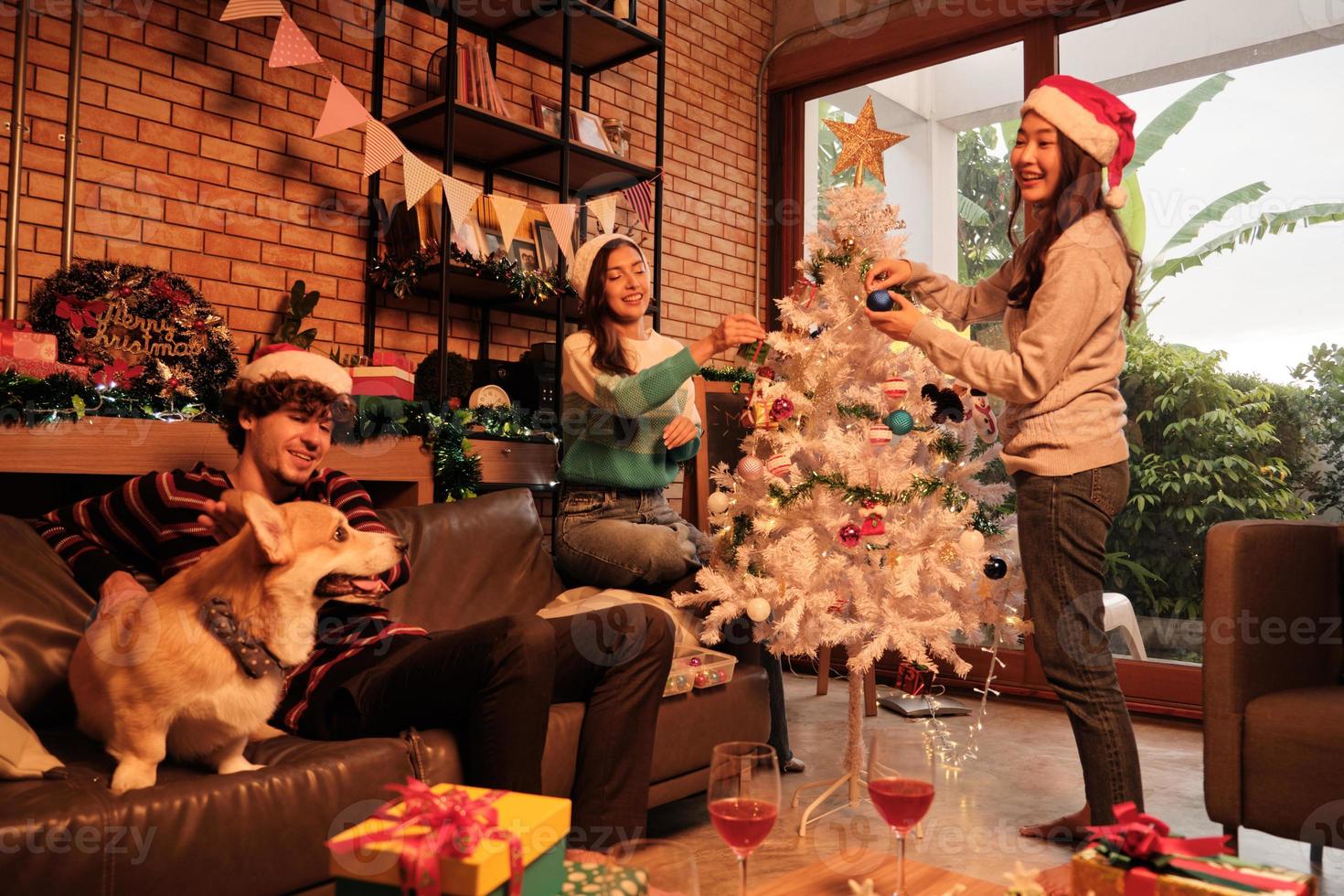 familia con perro y amigos juntos están decorando felizmente el árbol de Navidad blanco en la sala de estar de la casa, divertidos y alegres se preparan para una fiesta de celebración para el festival de año nuevo. foto