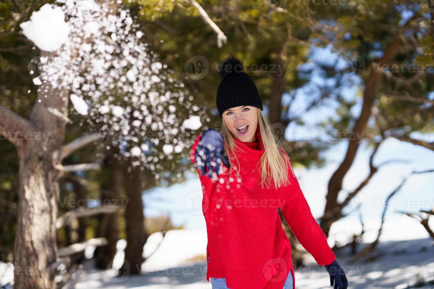 Young woman throwing snowballs forward in a snow-covered forest in the mountains photo