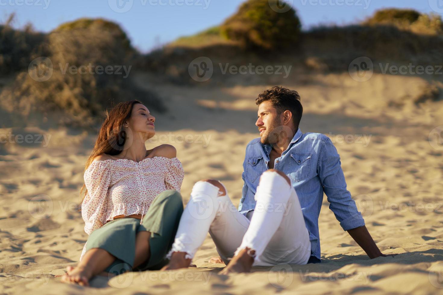 Feliz pareja amorosa sentada en la arena de la playa foto