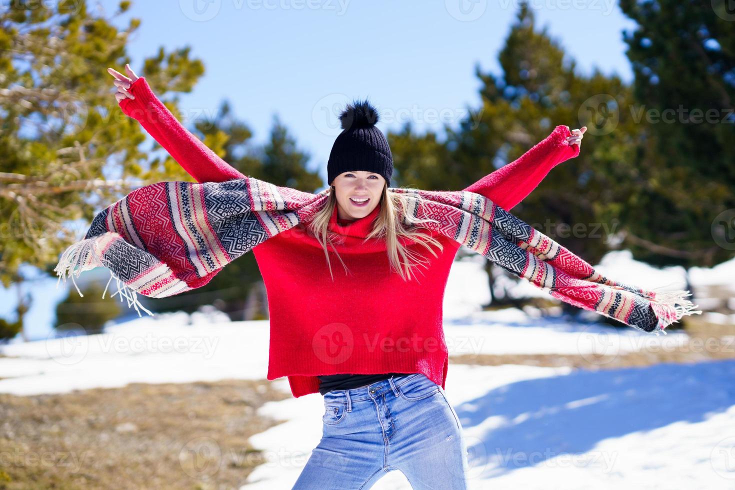 joven mujer rubia joven feliz agitando su bufanda en el viento en un bosque en las montañas nevadas. foto