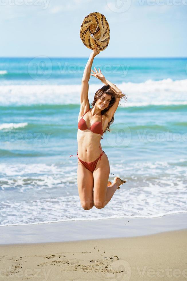 Young woman with beautiful body in swimwear jumping on a tropical beach. photo