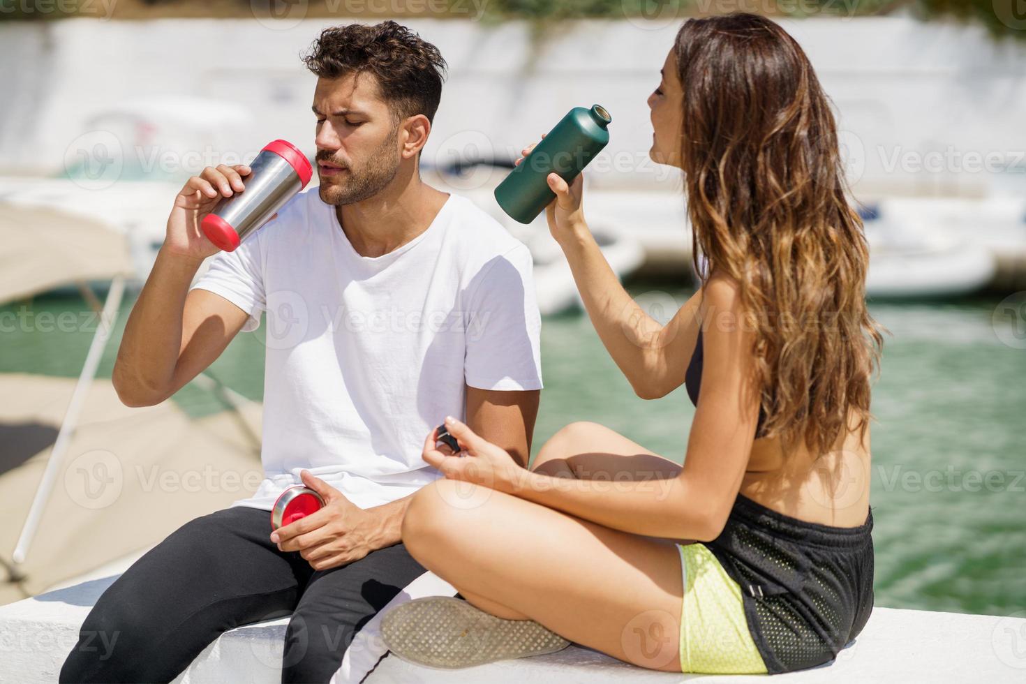 Joven pareja deportiva se hidrata con agua en latas de metal mientras se toma un descanso después del deporte. foto