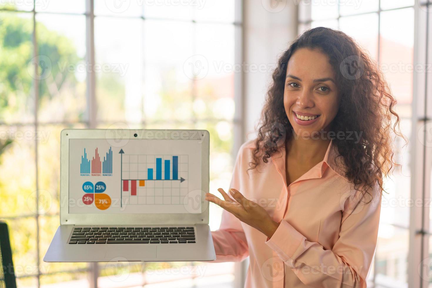 Mujer latina mostrando portátil con gráfico de negocios en pantalla foto