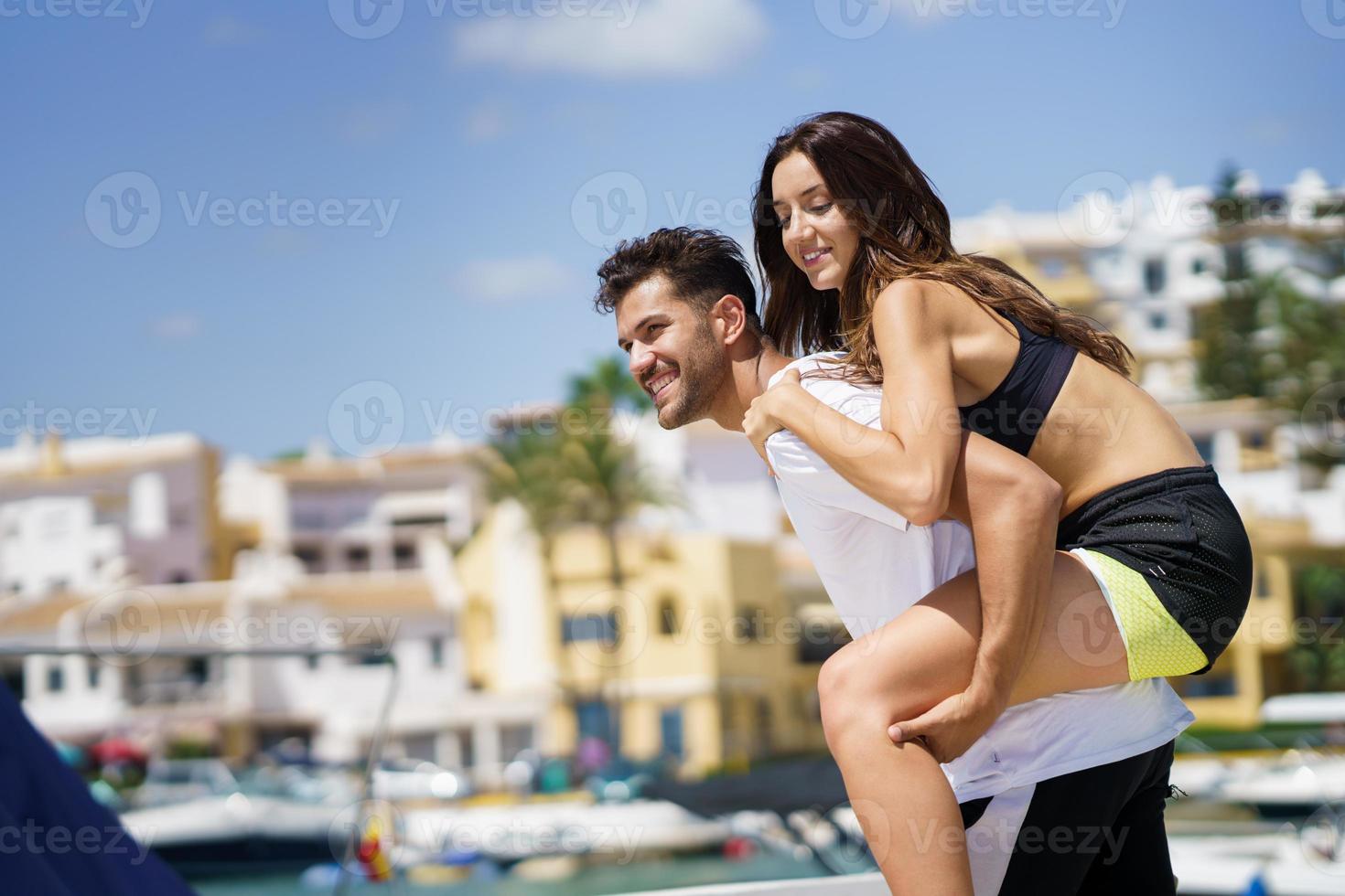 Man carrying his girlfriend on piggyback wearing sport clothes. photo