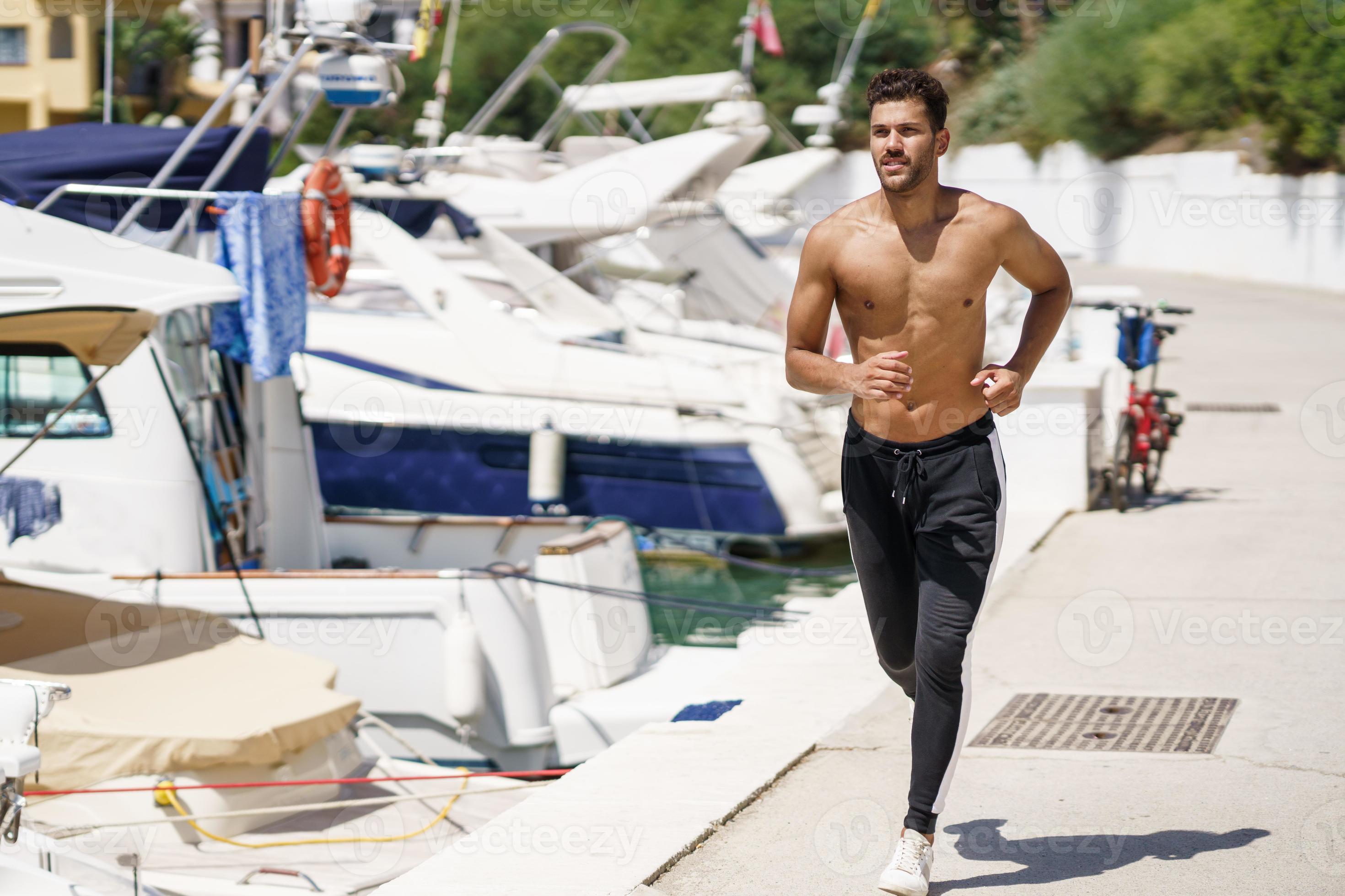 Young man with an athletic body running shirtless through a harbour. photo