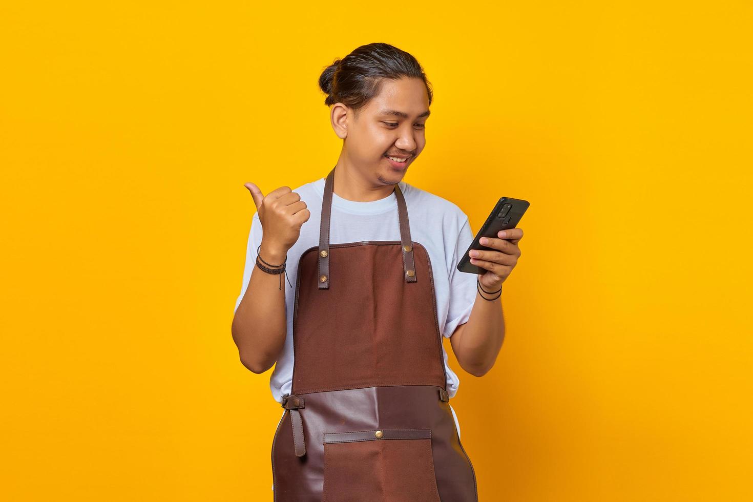 Retrato de hombre guapo alegre mirando el teléfono móvil con el dedo mostrando descuento de ventas sobre fondo amarillo foto