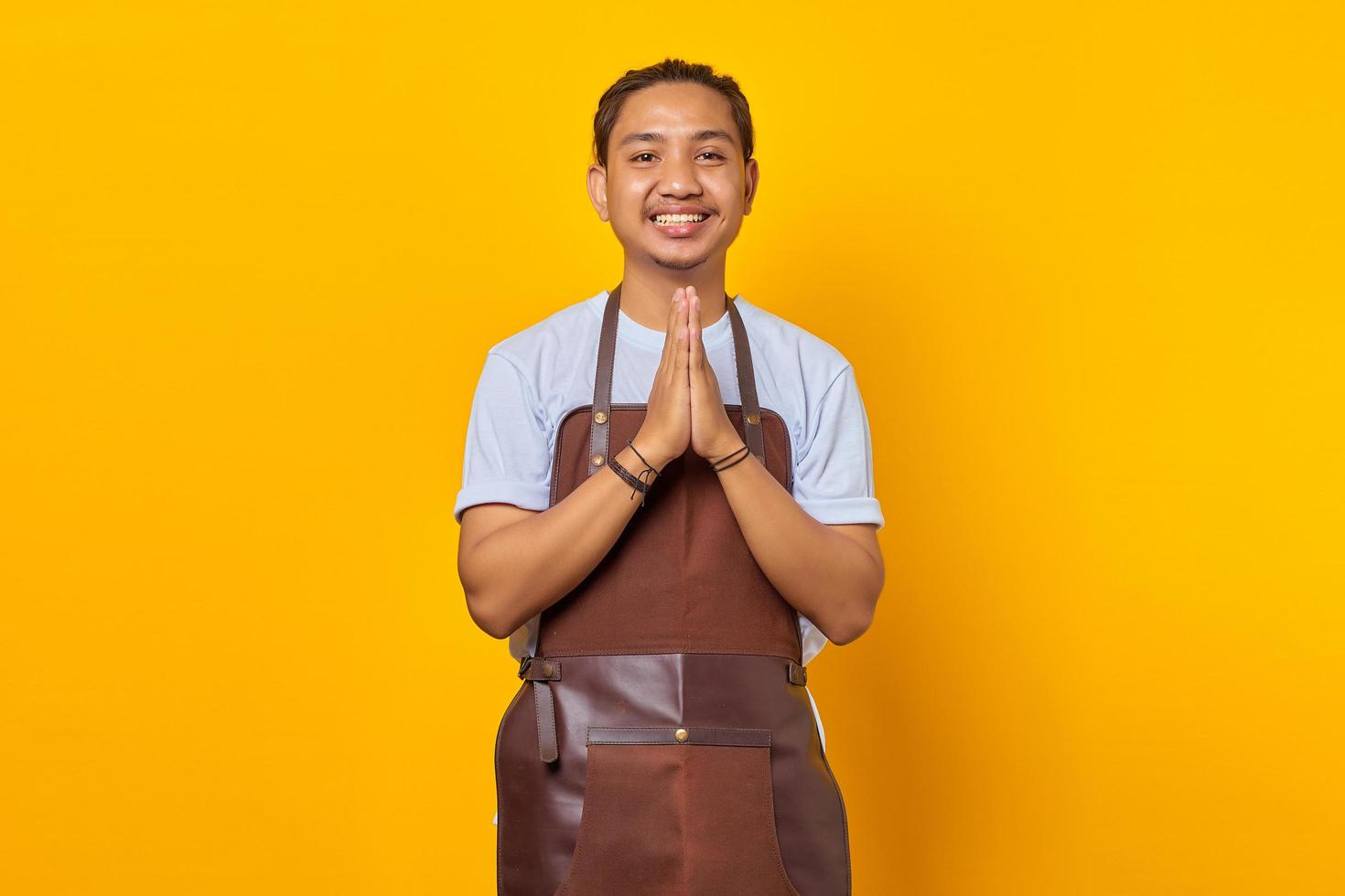 retrato, de, sonriente, guapo, asiático, joven, llevando, delantal, saludo, cliente, con, grande, sonrisa, en, el suyo, cara, aislado, en, fondo amarillo foto