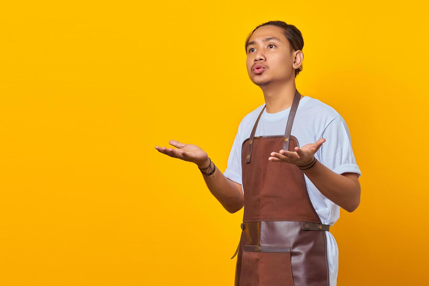 Portrait of surprised man barista with confused and displeased expression on yellow background photo