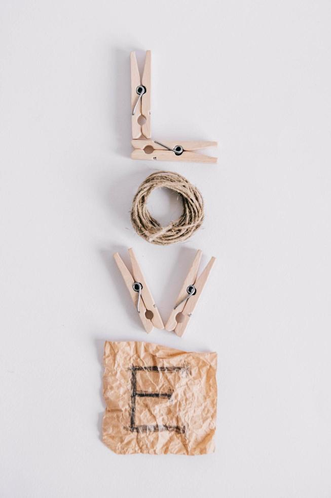 Inscription word love made of wooden clothespins, rope and brown paper sticker on white background. View from above. Place for your text photo