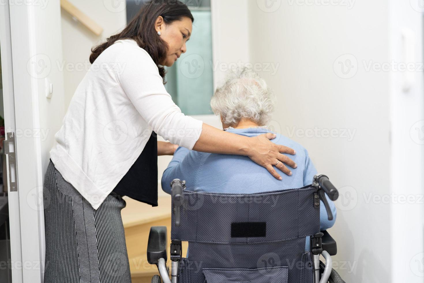cuidador ayuda a anciana asiática o anciana sentada en silla de ruedas para subir las escaleras en casa. foto