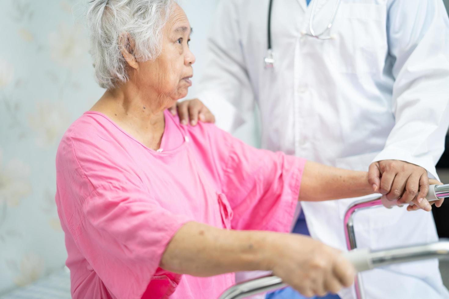 Asian nurse physiotherapist doctor care, help and support senior or elderly old lady woman patient walk with walker at hospital ward, healthy strong medical concept. photo