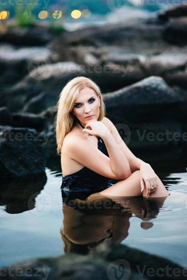 blonde girl in a black dress with blue eyes on the coast of the river photo