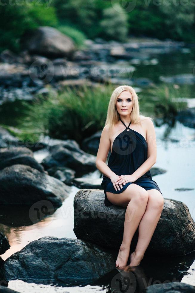 blonde girl in a black dress with blue eyes on the coast of the river photo